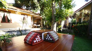 A wooden table with two cushioned seating areas in a garden setting. - Barbados Terrace (Rayong)