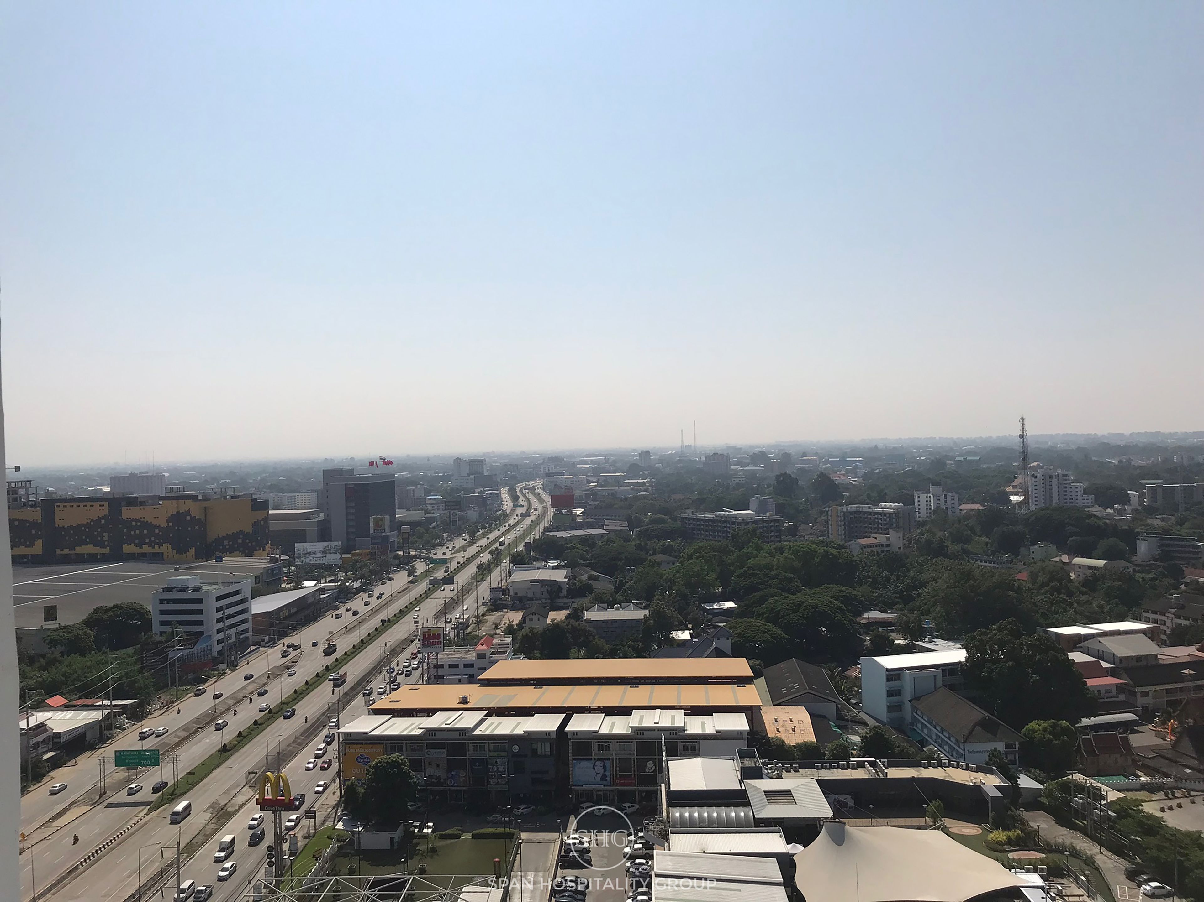 Une vue urbaine mettant en scène un bâtiment imposant, doté d’un toit plat et de nombreuses fenêtres, entouré d’autres bâtiments et bordé par une rue animée.