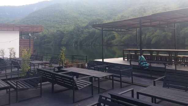 An outdoor seating area with benches and tables, overlooking a river and forested hills. - Ingphupha Resort and Restaurant (Si Sawat)