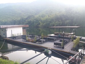 A lakeside deck with tables and benches, surrounded by lush greenery and a calm lake. - Ingphupha Resort and Restaurant (Si Sawat)