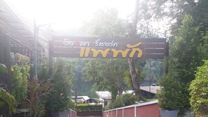 A garden entrance with a sign in a foreign language, surrounded by potted plants and trees. - Ingphupha Resort and Restaurant (Si Sawat)