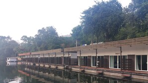 A row of modern, single-story buildings with large windows and a covered walkway over a calm body of water. - Ingphupha Resort and Restaurant (Si Sawat)