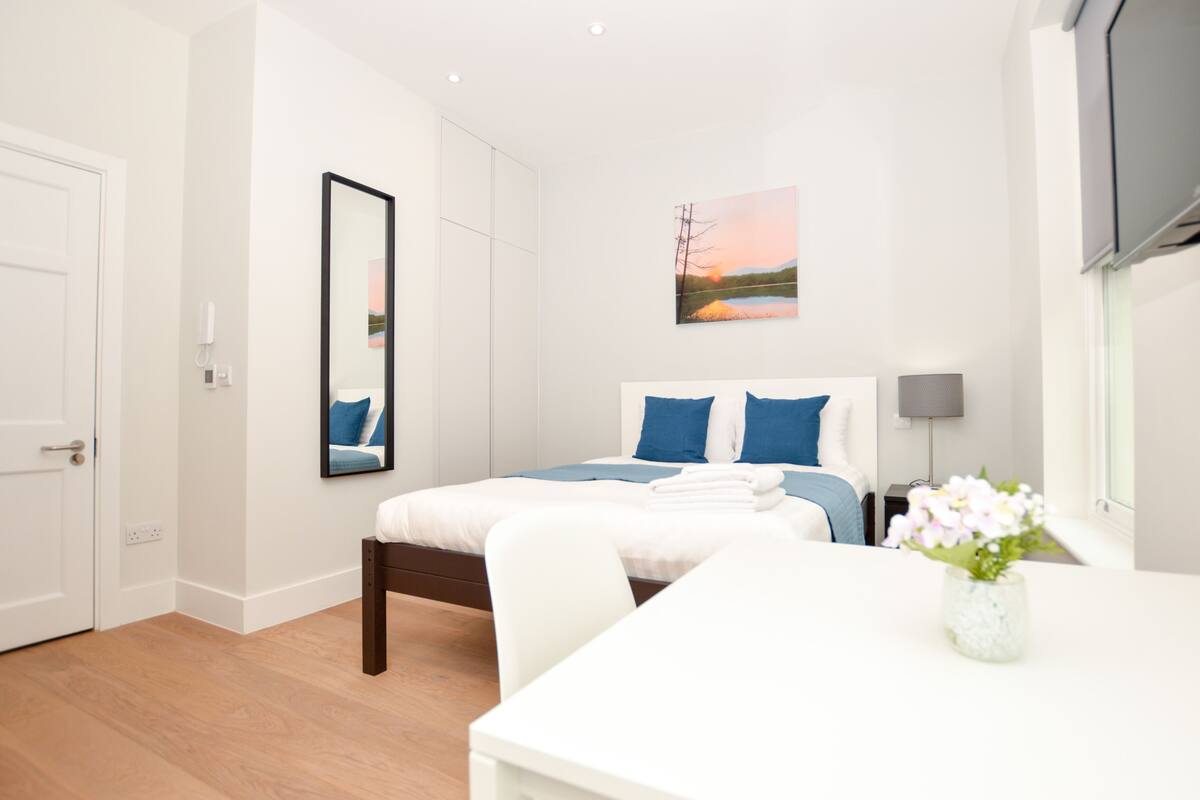 A modern hotel room with a bed, bedside table, and a painting of a sunset.