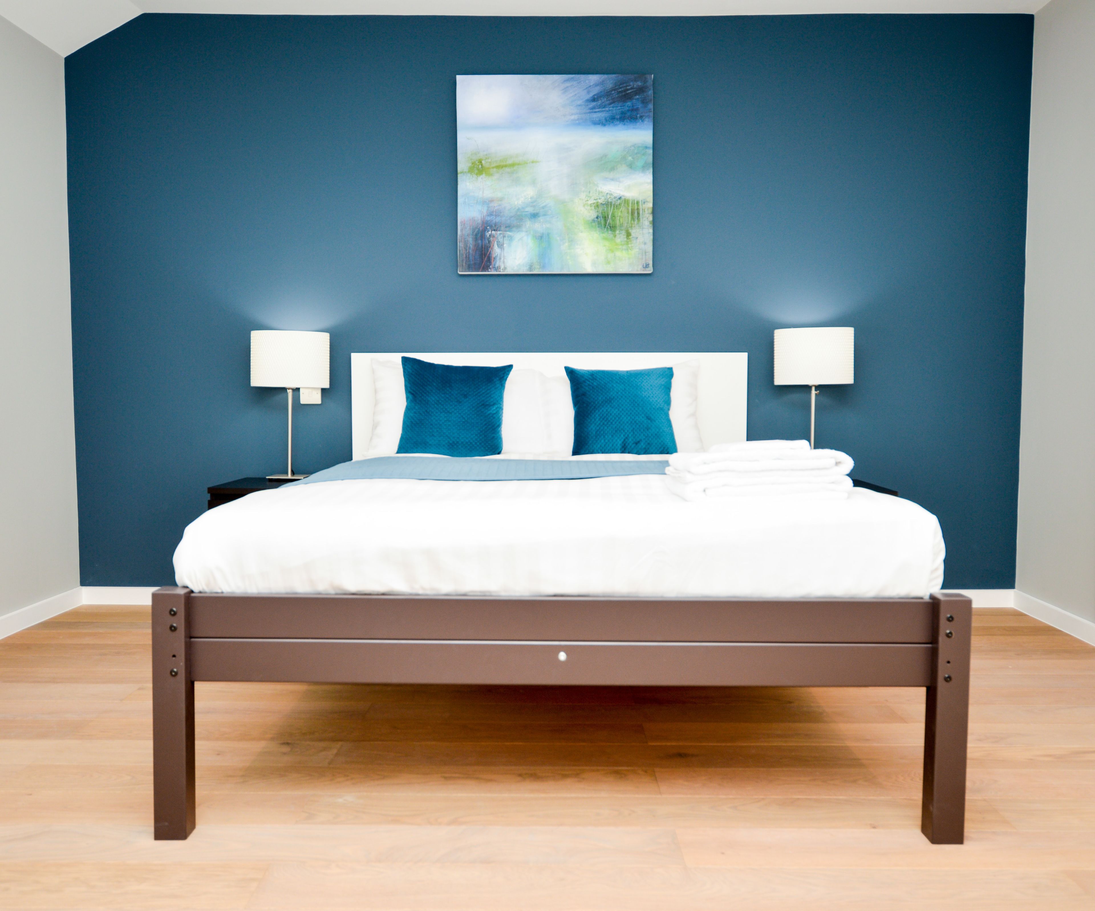 A modern bedroom with a bed, two bedside lamps, and a painting on the wall.