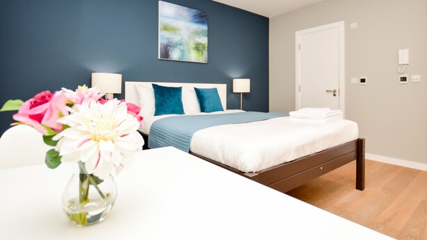 A modern bedroom with a bed, bedside tables, a vase with flowers, and a painting on the wall. - Fitzroy Serviced Apartments by Concept Apartments (London)