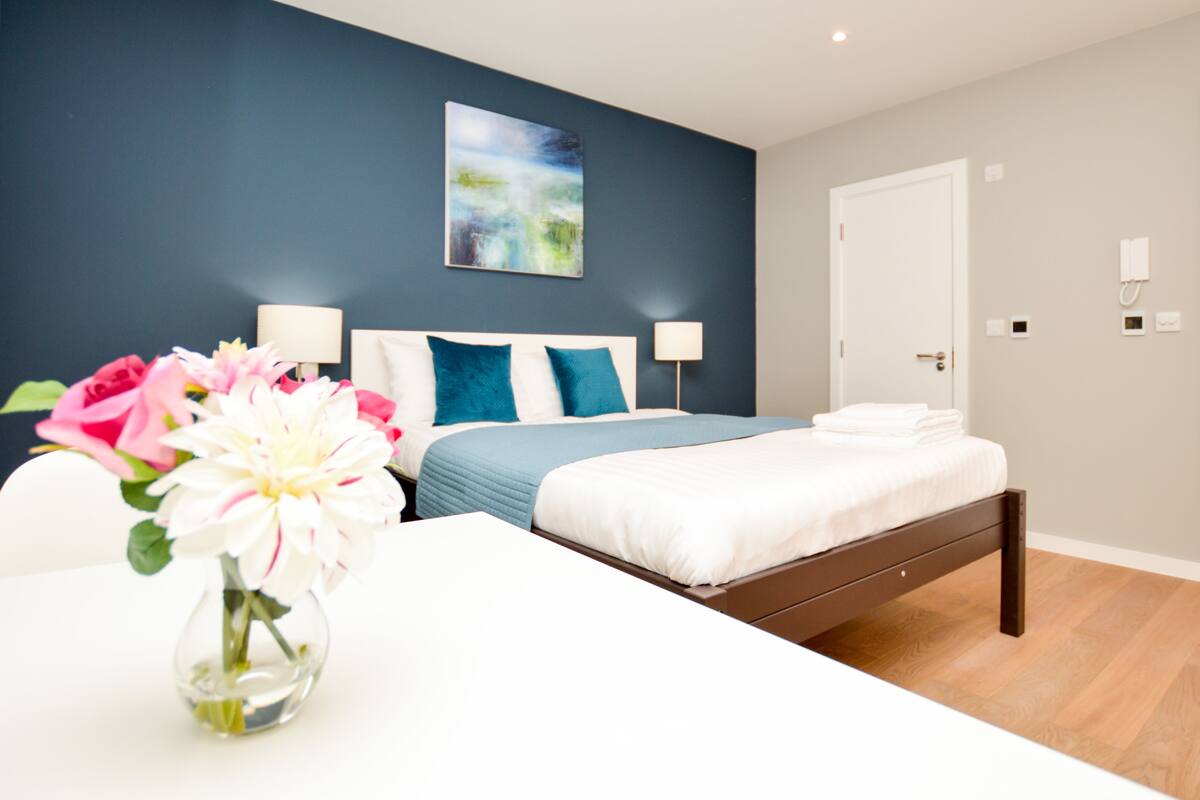 A modern bedroom with a bed, bedside tables, a vase with flowers, and a painting on the wall.