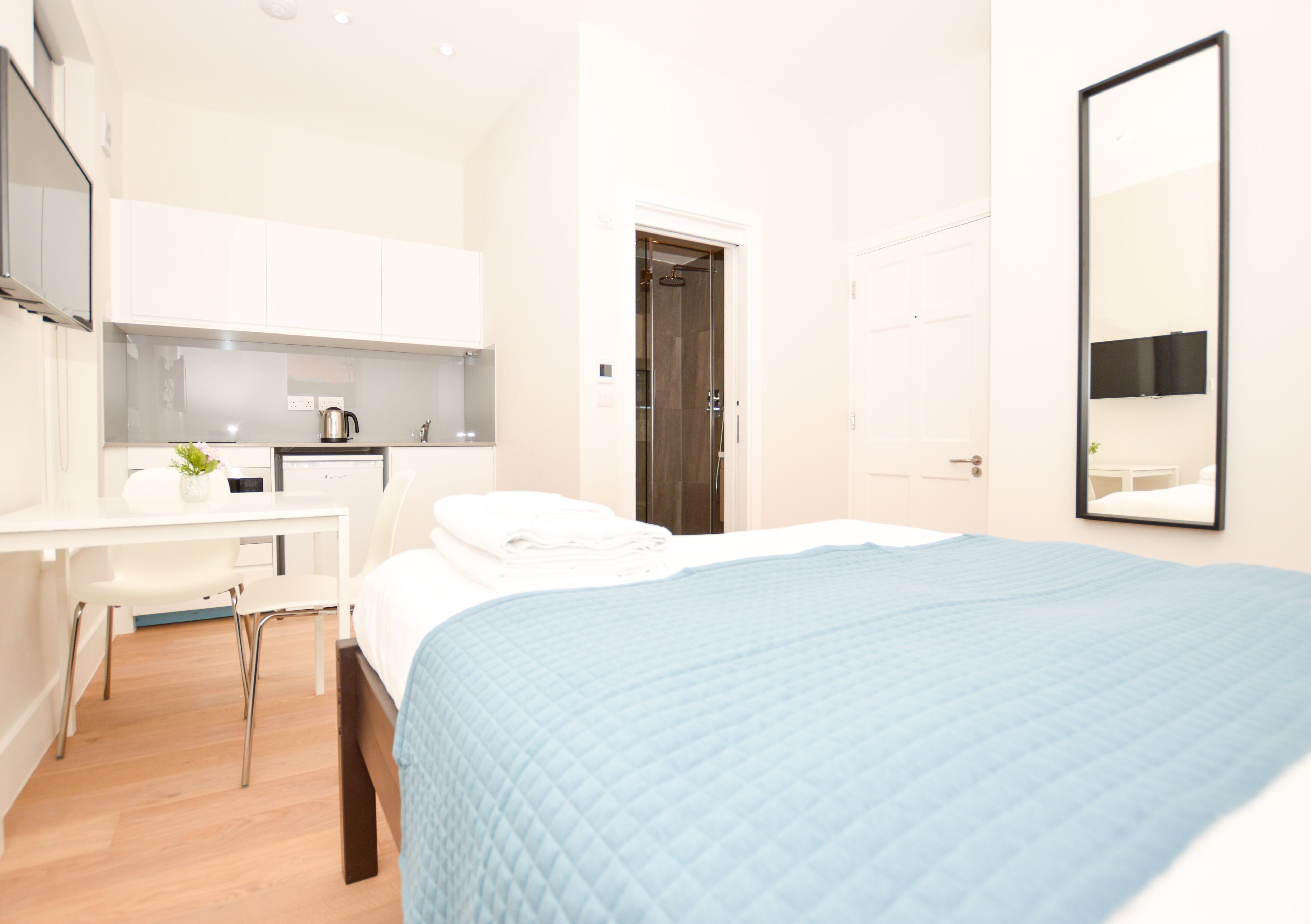 A hotel room with a bed, a desk, a chair, a mirror, and a door.