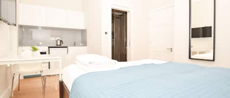 A hotel room with a bed, a desk, a chair, a mirror, and a door.