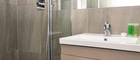Un baño moderno con ducha de vidrio, un lavabo blanco y un espejo encima.