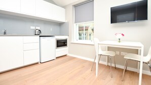 A modern kitchen with white cabinets, a built-in oven, and a coffee maker. There is a window with a view of a building outside. - Fitzroy Serviced Apartments by Concept Apartments (London)