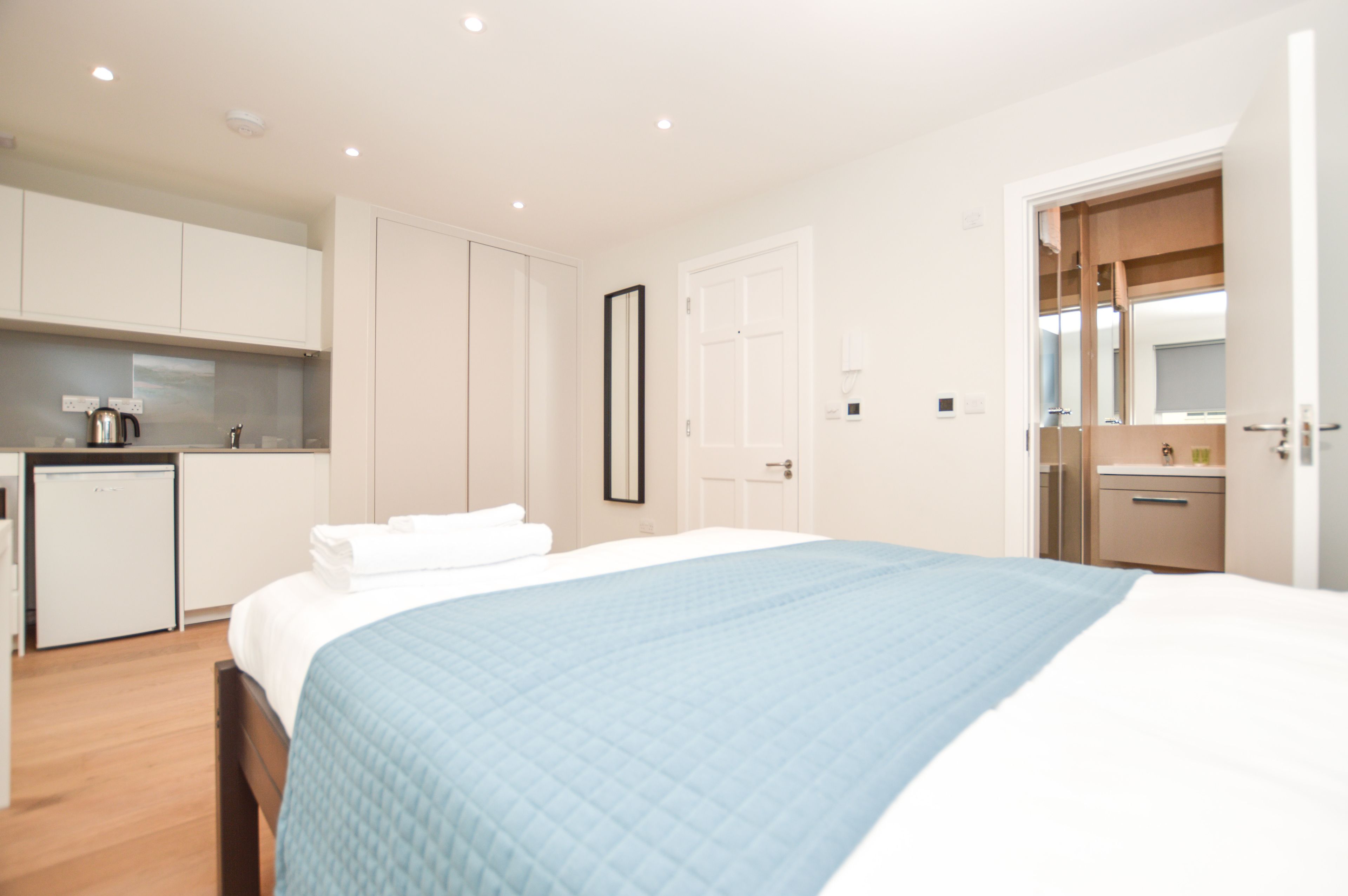 A modern hotel room with a large bed, a separate bathroom, a kitchenette, and a walk-in closet.