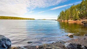 A calm lake with clear water, surrounded by a forest and rocky shoreline.