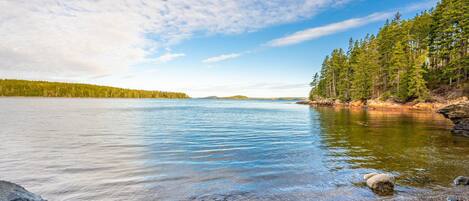 A calm lake with clear water, surrounded by a forest and rocky shoreline.