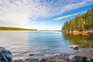 A calm lake with clear water, surrounded by a forest and rocky shoreline.
