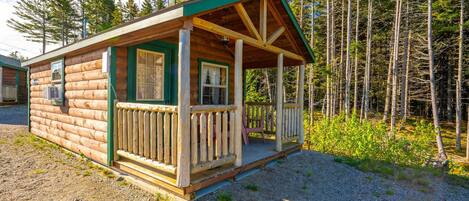 Une cabane en rondins dotée d’une véranda, entourée d’arbres.