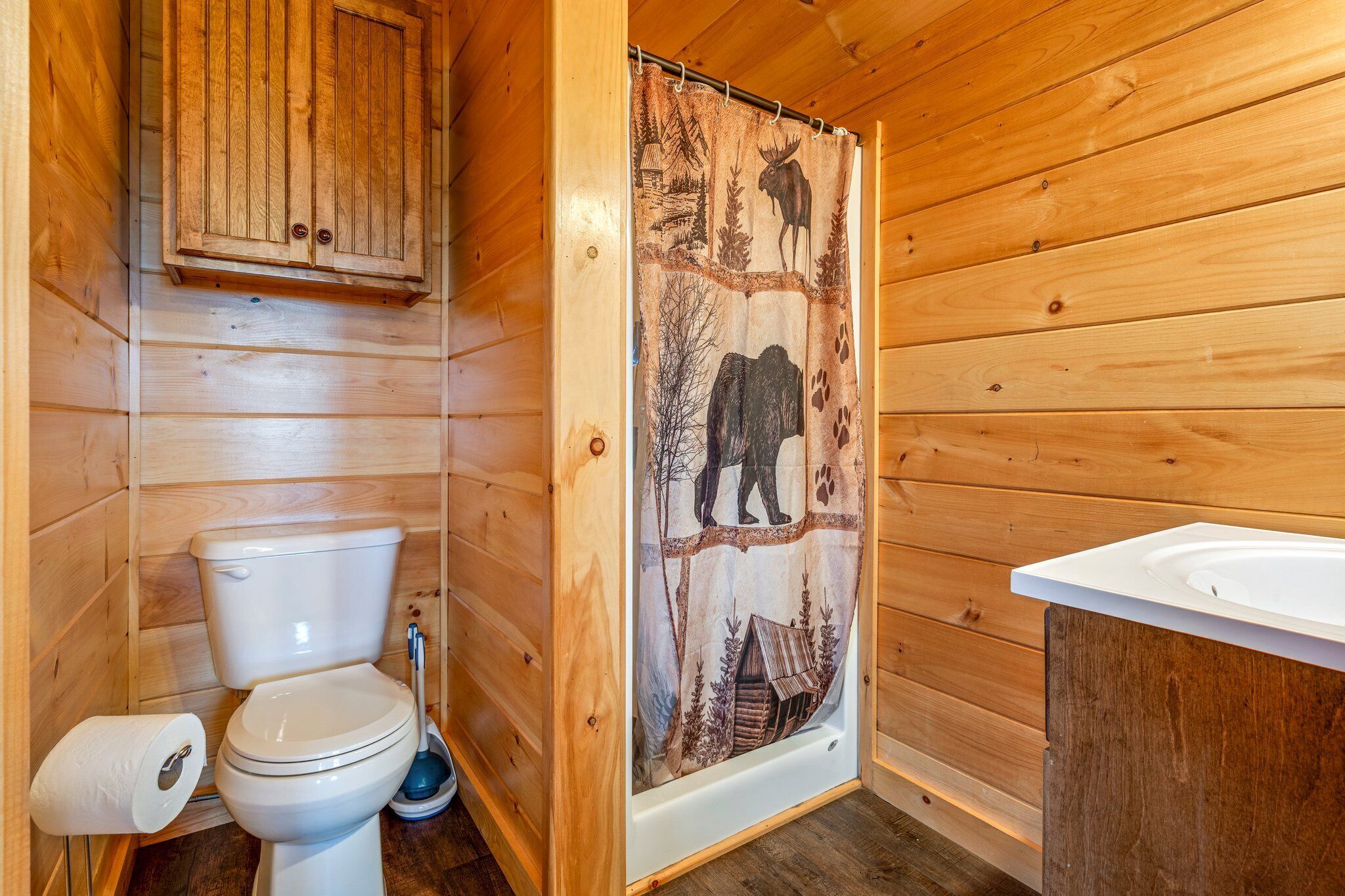 Ein Badezimmer einer Holzhütte mit Toilette, einer Duschkabine mit Tierdrucken und einem Holzschrank über der Toilette.