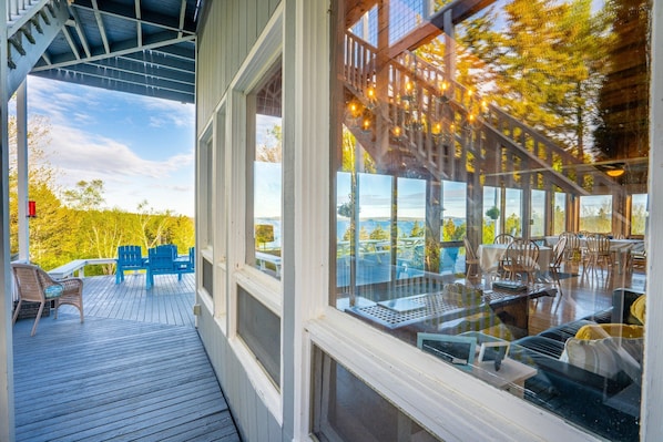 A covered outdoor deck with blue Adirondack chairs, a table, and a sofa. - Bluff House Inn (Gouldsboro)