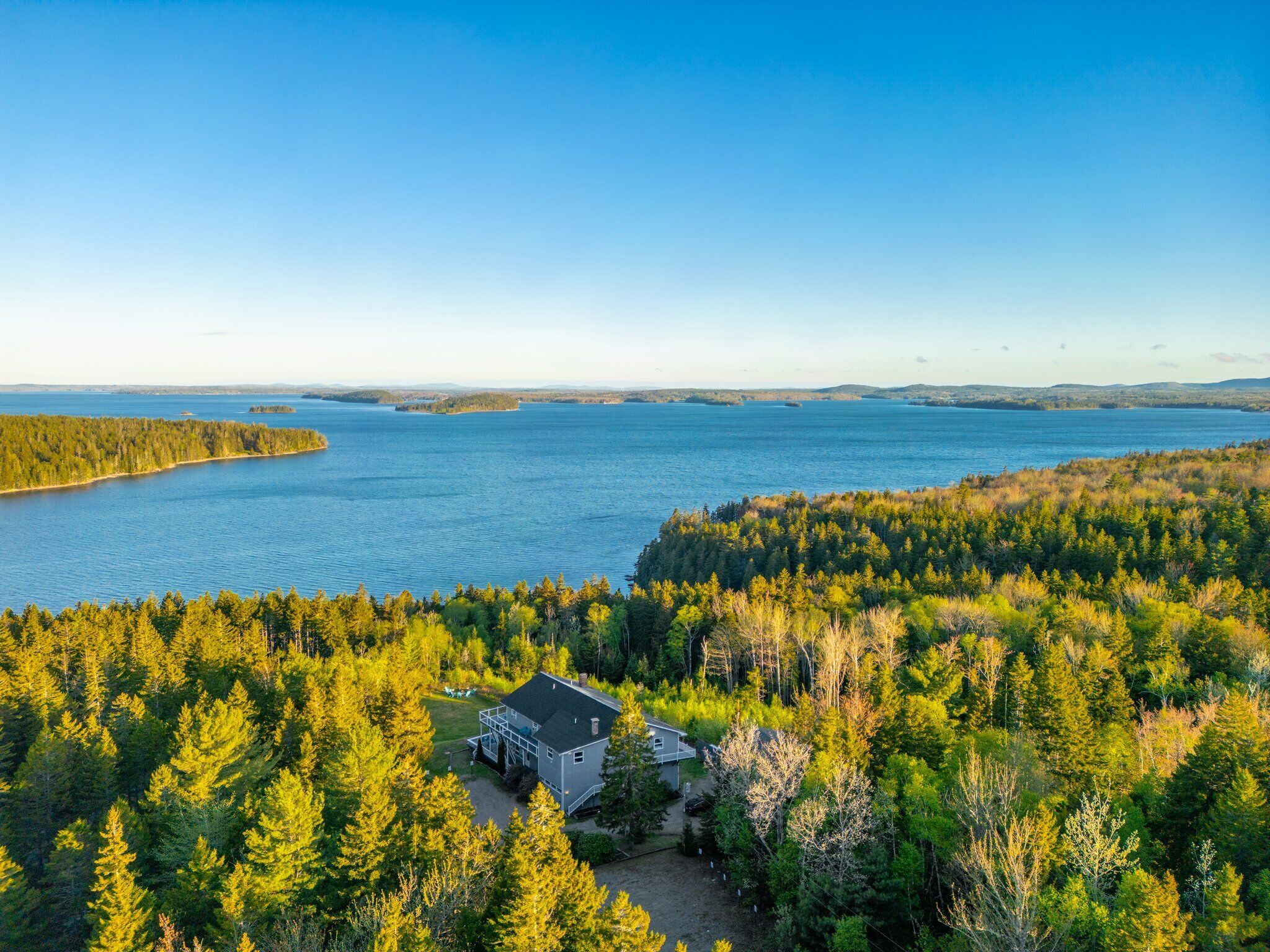A house surrounded by dense forest with a view of a large body of water.