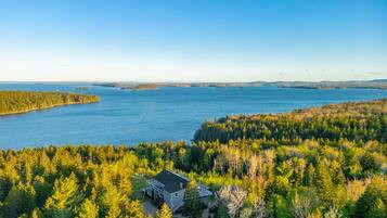 A house surrounded by dense forest with a view of a large body of water.