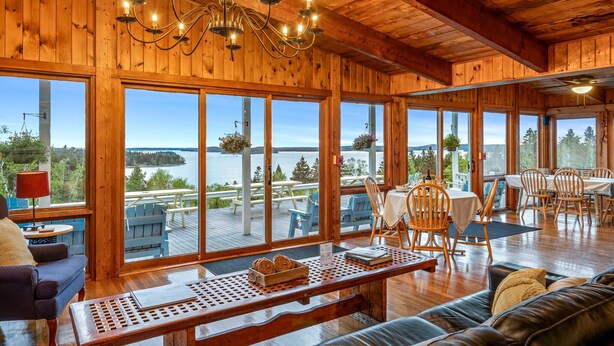 A wooden cabin with large windows overlooking a lake, furnished with a sofa, dining table, and chairs. - Bluff House Inn (Gouldsboro)