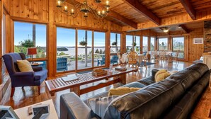 A spacious room with wooden walls and large windows, a chandelier, and a dining area with outdoor seating. - Bluff House Inn (Gouldsboro)