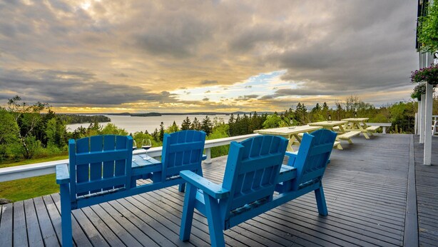 A deck with blue Adirondack chairs and a picnic table overlooking a lake.