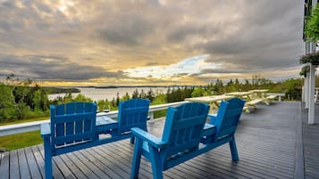A deck with blue Adirondack chairs and a picnic table overlooking a lake.