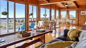 A wooden cabin with large windows, a dining area, and a cozy seating area with a sofa and a table. - Bluff House Inn (Gouldsboro)