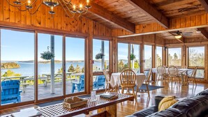 A wooden cabin with large windows overlooking a lake, furnished with a couch, dining table, and chairs. - Bluff House Inn (Gouldsboro)