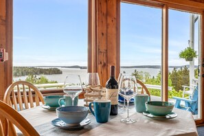 A table set with blue bowls, wine glasses, and a bottle of wine, overlooking a scenic view of a lake and forest. - Bluff House Inn (Gouldsboro)