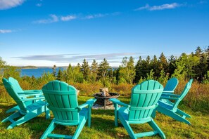 Two turquoise Adirondack chairs facing a fire pit with a view of a lake and forest.