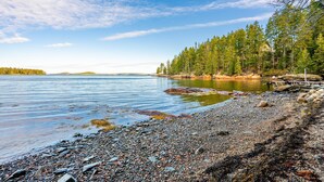 A rocky shoreline with a calm lake, surrounded by dense forest and a clear sky. - Bluff House Inn (Gouldsboro)