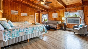 A wooden cabin with a bed, a sofa, a chair, and a window with curtains.