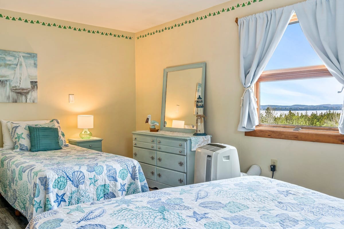 Un dormitorio con dos camas, un tocador, un espejo, una lámpara y una ventana con cortinas.