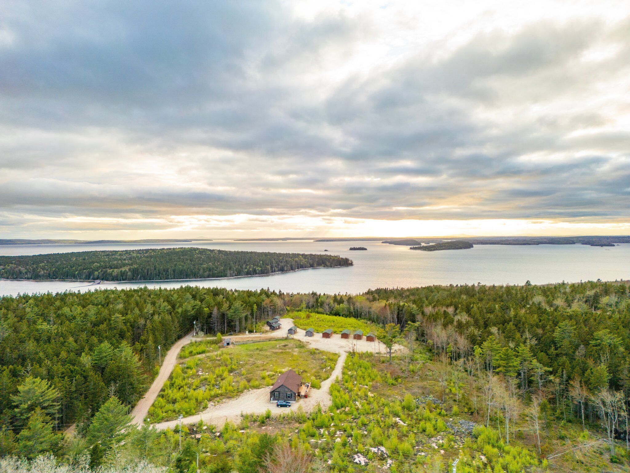 A remote cabin surrounded by dense forest, with a view of a large body of water and distant islands.