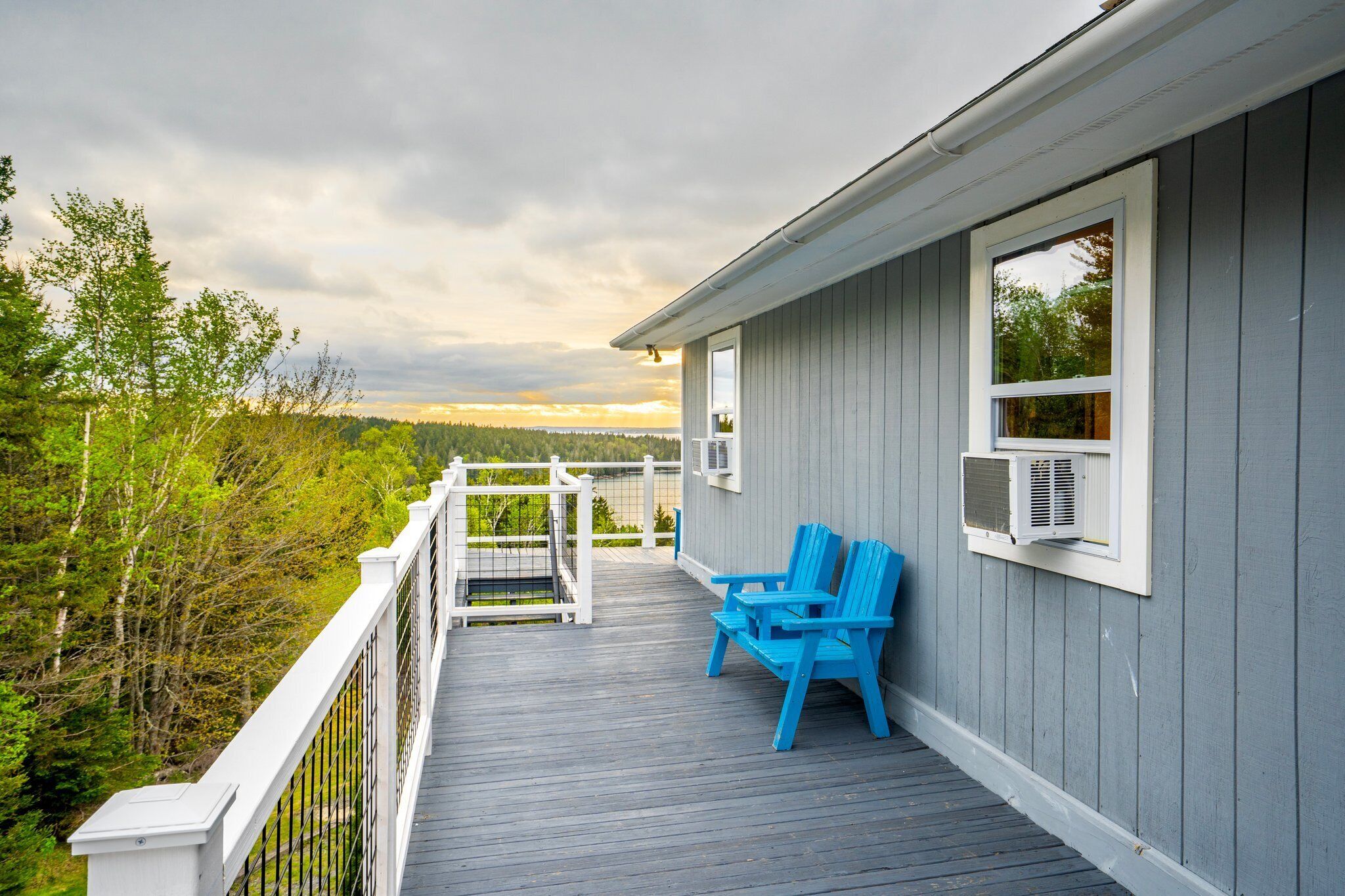 A deck with blue Adirondack chairs, a white railing, and a view of a forested area.