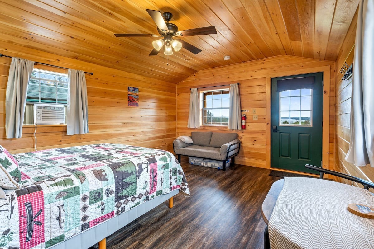 Una habitación de cabaña acogedora con una cama, un sofá, una mesa y una puerta que da al exterior.