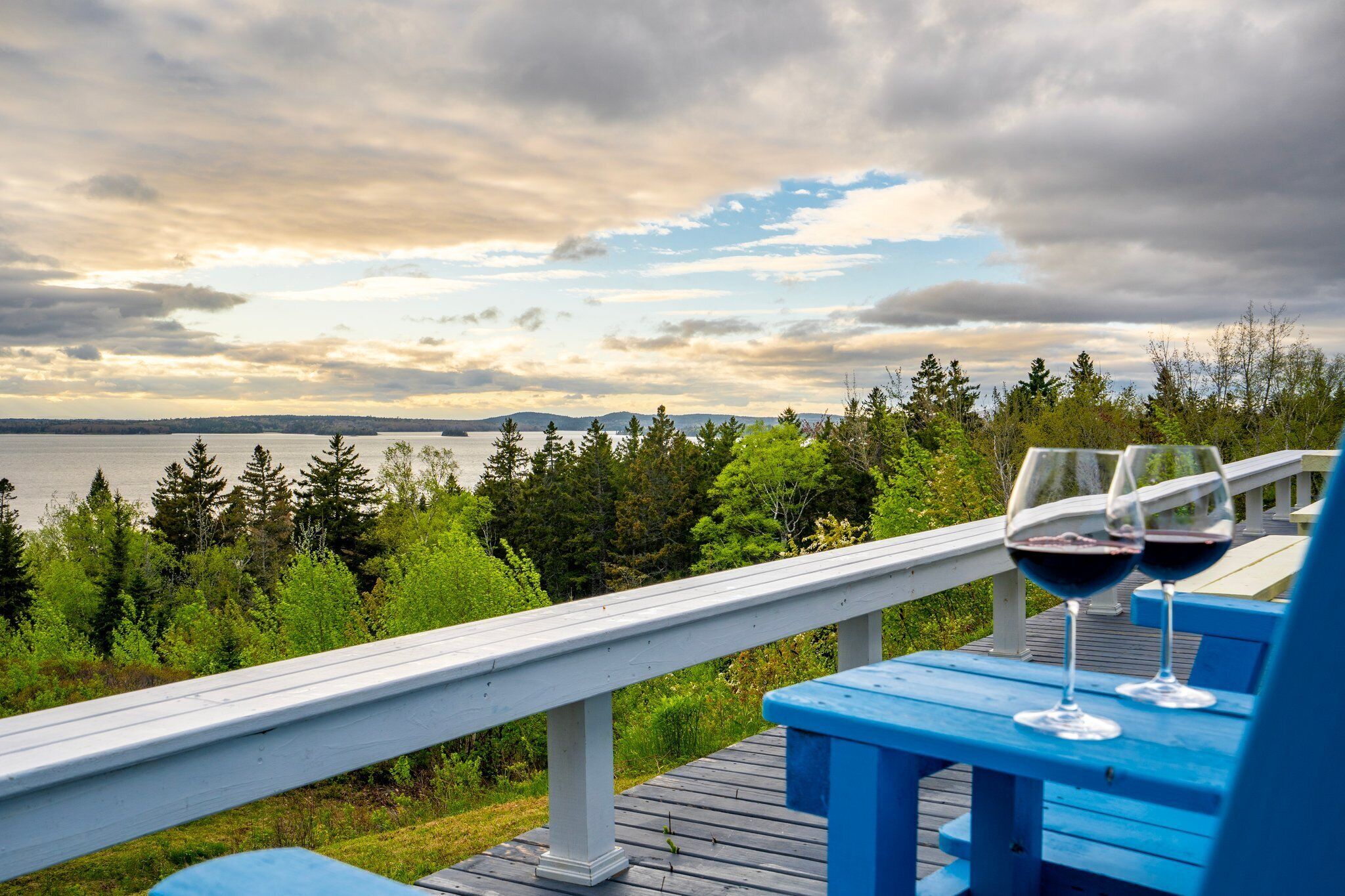 A wooden deck with a railing overlooking a body of water and forested area.