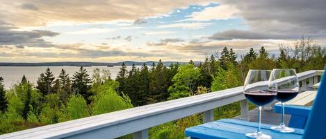 A wooden deck with a railing overlooking a body of water and forested area.