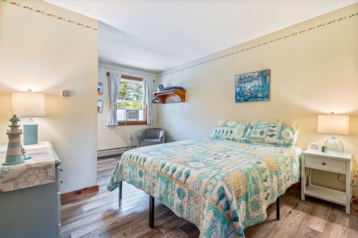 Un dormitorio con cama, mesita de noche, lámpara, cómoda y ventana con cortinas.