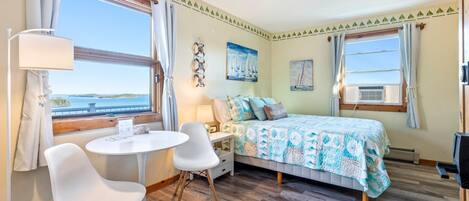 Une chambre avec un lit, une table, deux chaises, une lampe et une vue sur la mer.