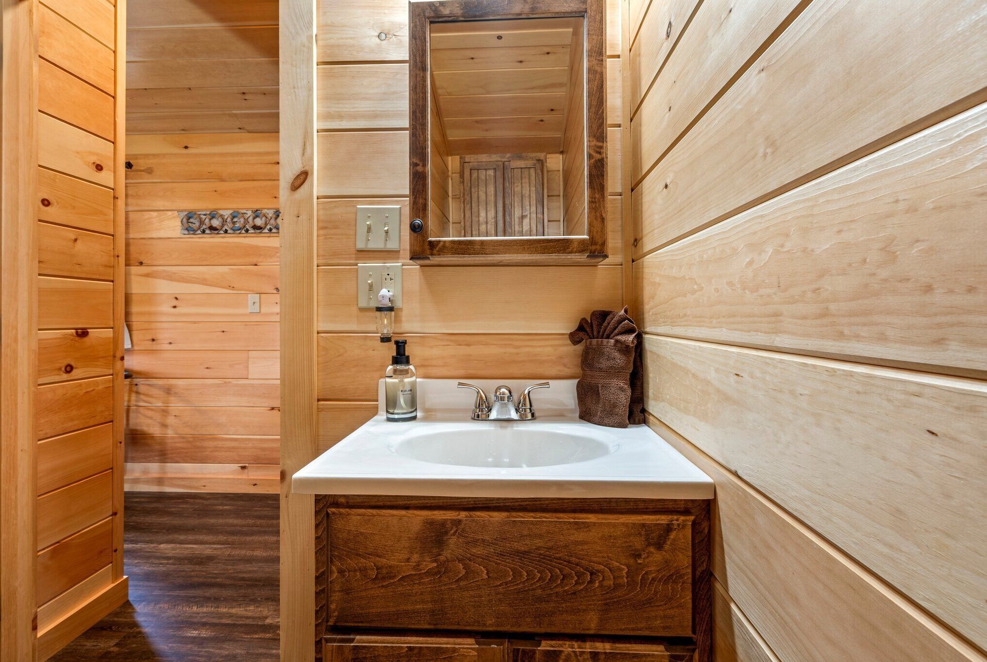 A wooden bathroom with a sink, mirror, and towel rack.