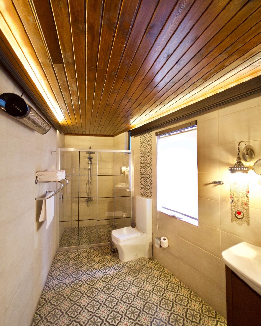 Een badkamer met douche, toilet en wastafel, met behangtegels en een houten plafond.