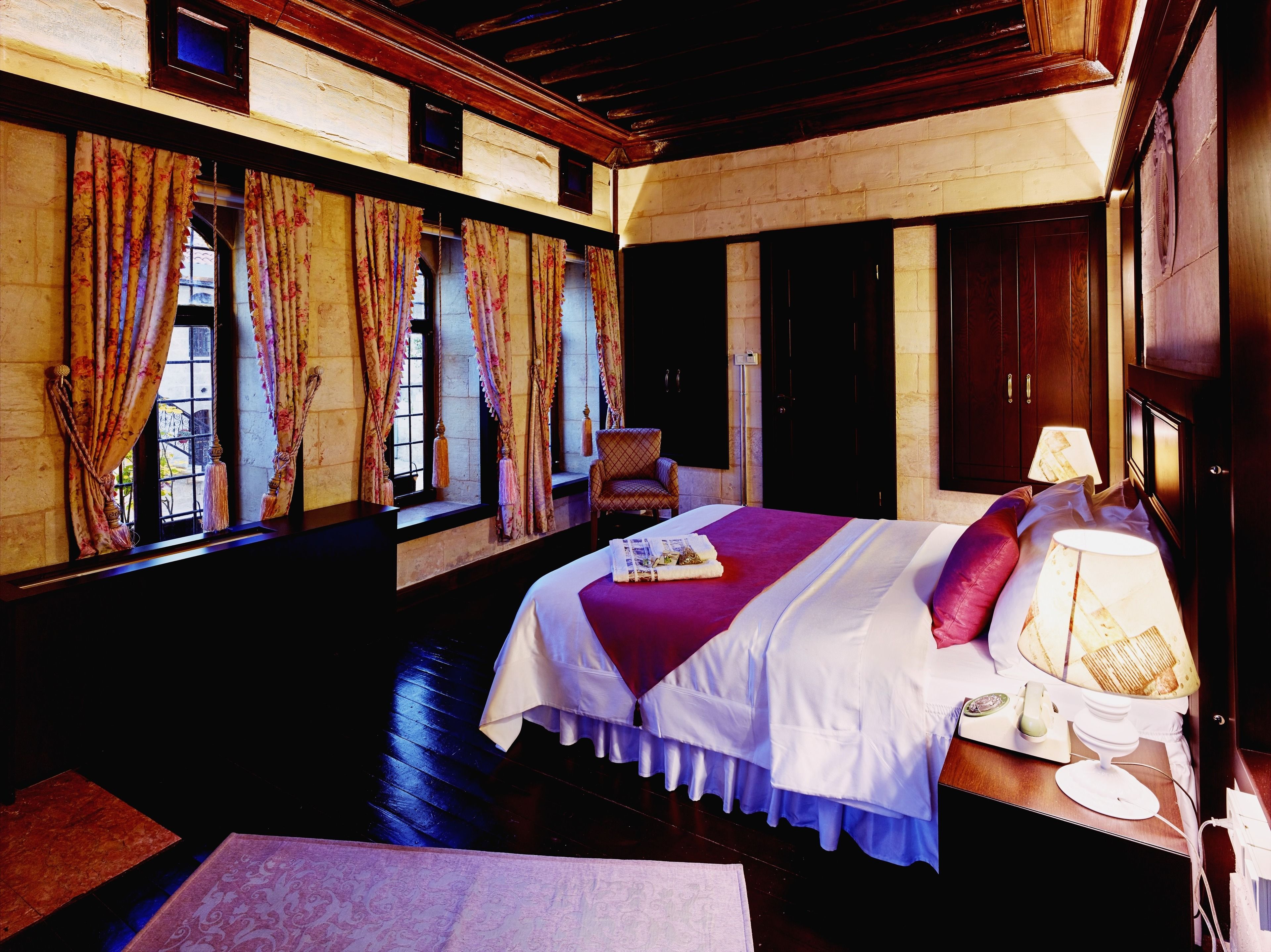 A hotel room with a large bed, a chair, a desk with a lamp, and curtains on the windows.