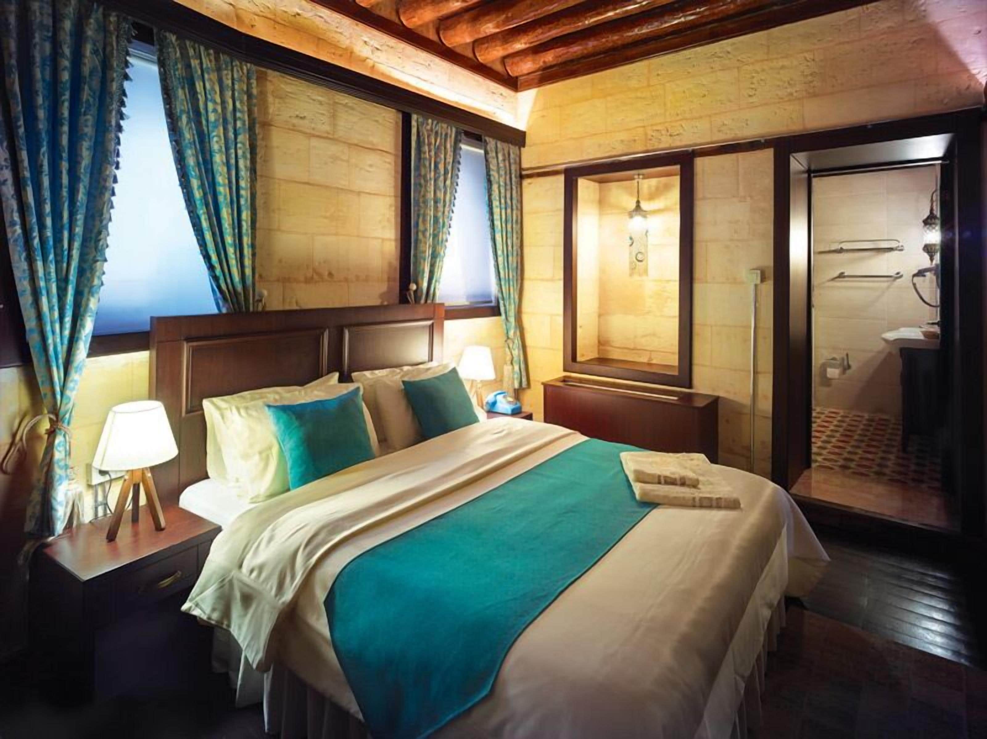A hotel room with a large bed, wooden headboard, two bedside lamps, a nightstand, and a view of the bathroom.