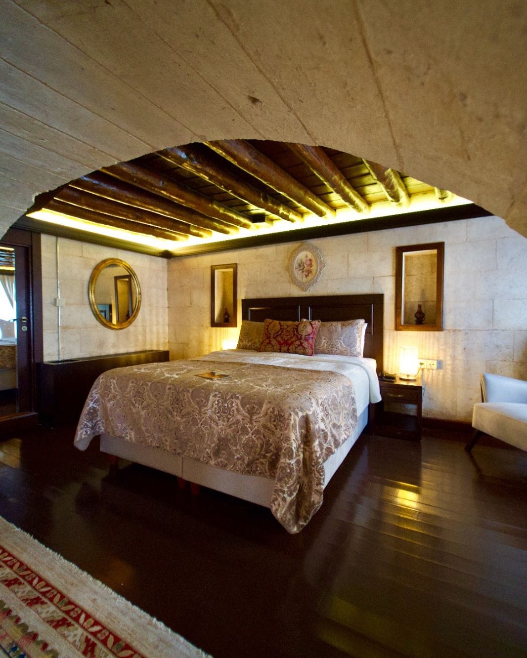 Un dormitorio con una cama grande, techo de madera, un espejo redondo y una mesita de noche con lámpara.