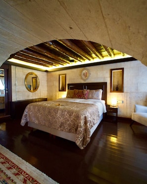 Un dormitorio con una cama grande, techo de madera, un espejo redondo y una mesita de noche con lámpara.
