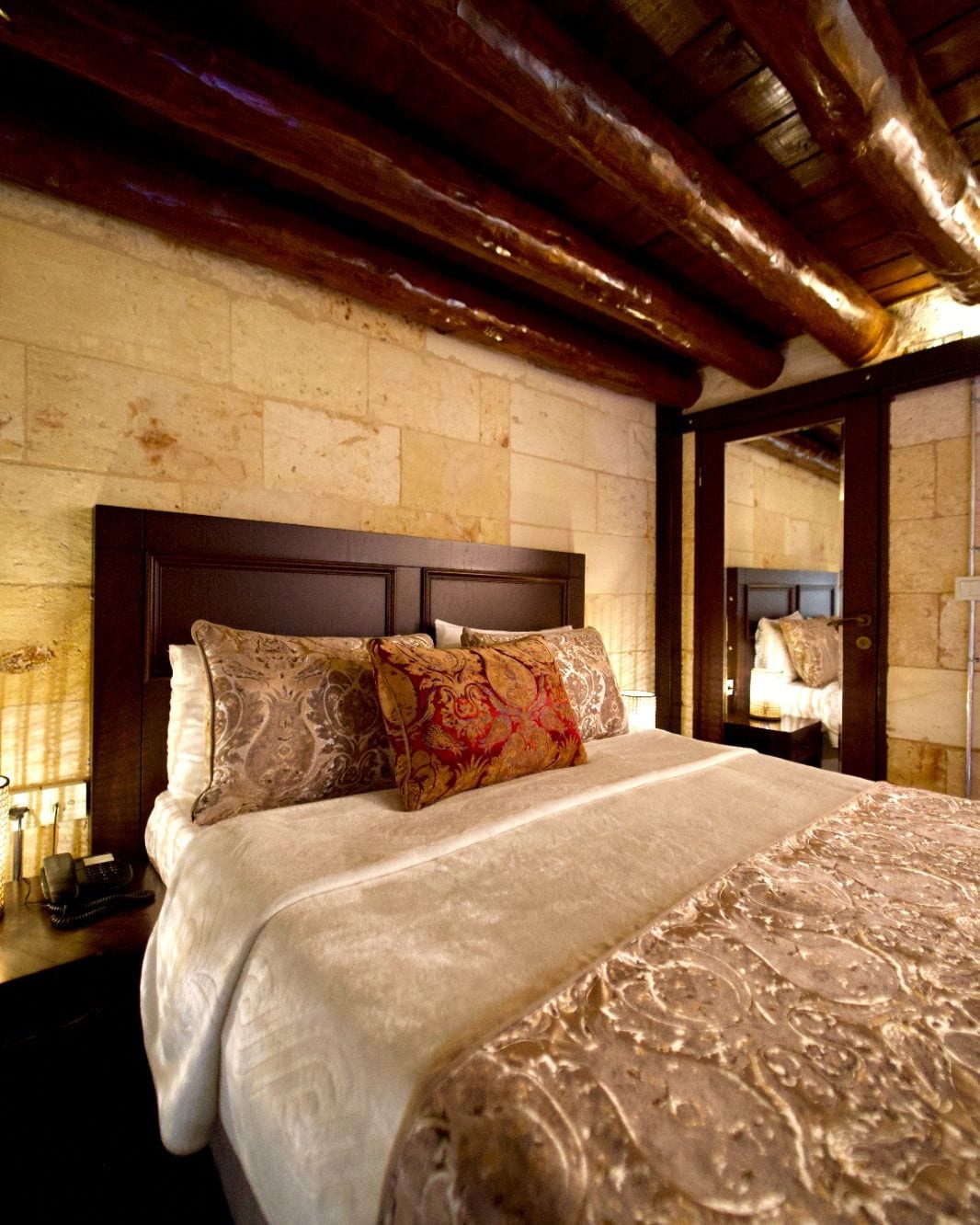 A hotel room with a large bed, a wooden headboard, and a stone wall.