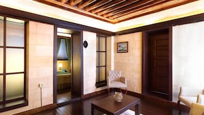 Una habitación con piso de madera, una mesa oscura de madera, un sofá color beige y una silla. Hay un cuadro en la pared y una puerta con marco de madera.