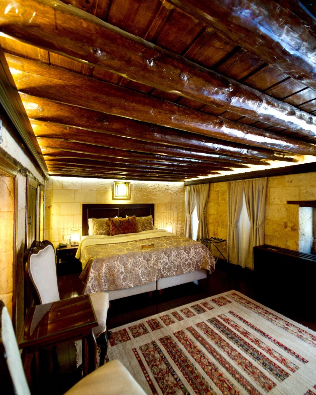 Ein Zimmer mit Holzboden, einem Bett mit gemustertem Bettbezug, einem Nachttisch und einem Sessel.